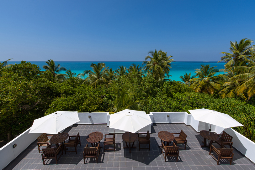Boutique Beach Hotel Roof Terrace with Tables, Chairs, White Umbrellas and Azure Blue Ocean in the Background